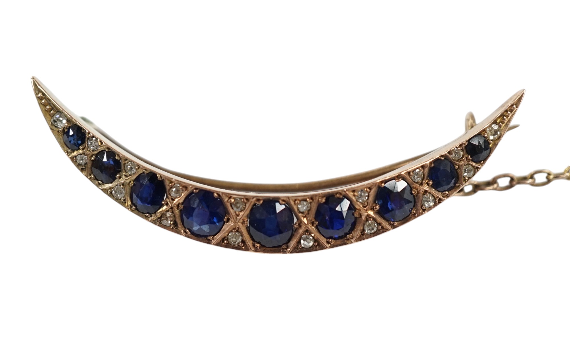 An early 20th century yellow metal, graduated sapphire set crescent brooch, with diamond chip spacers, 49mm, gross weight 5.8 grams. Condition - fair to good